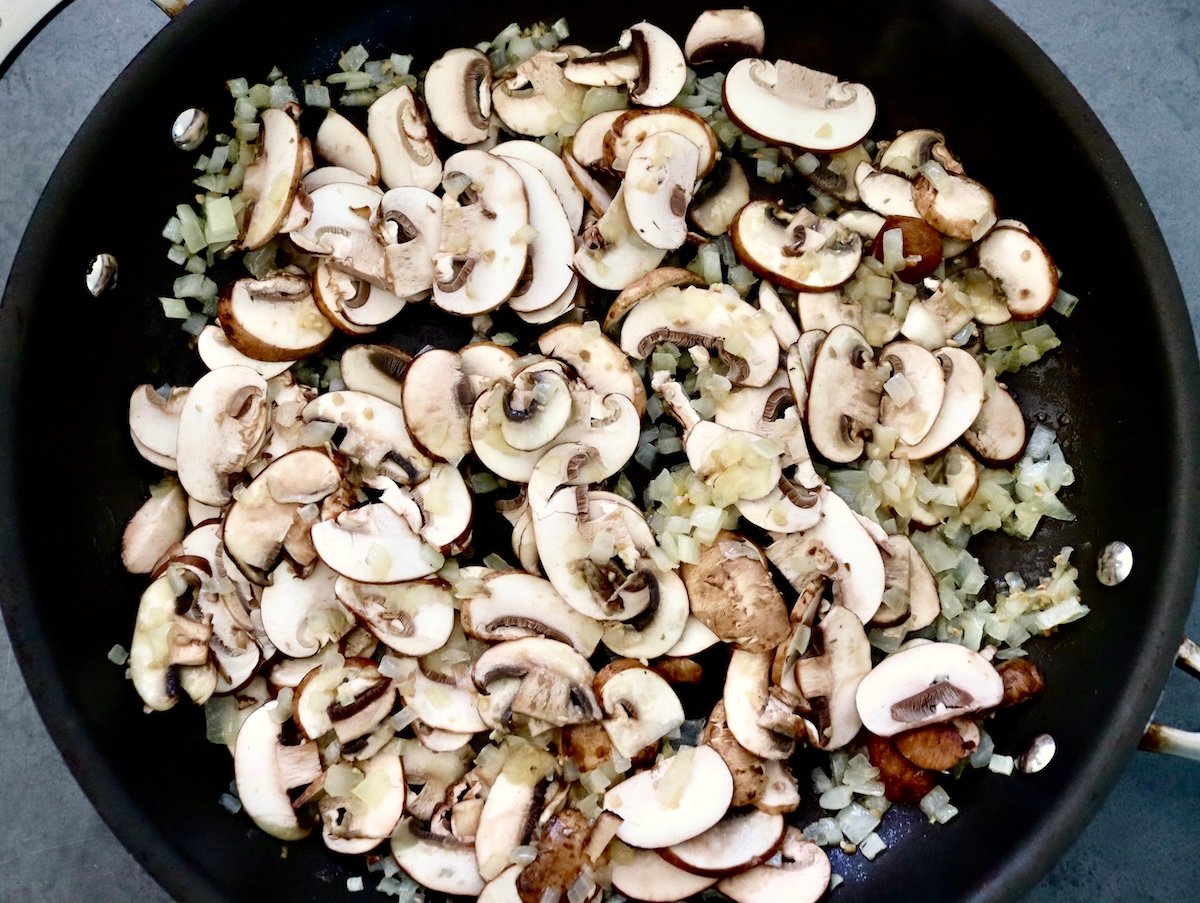 Skillet filled with chopped mushrooms and chopped onions.