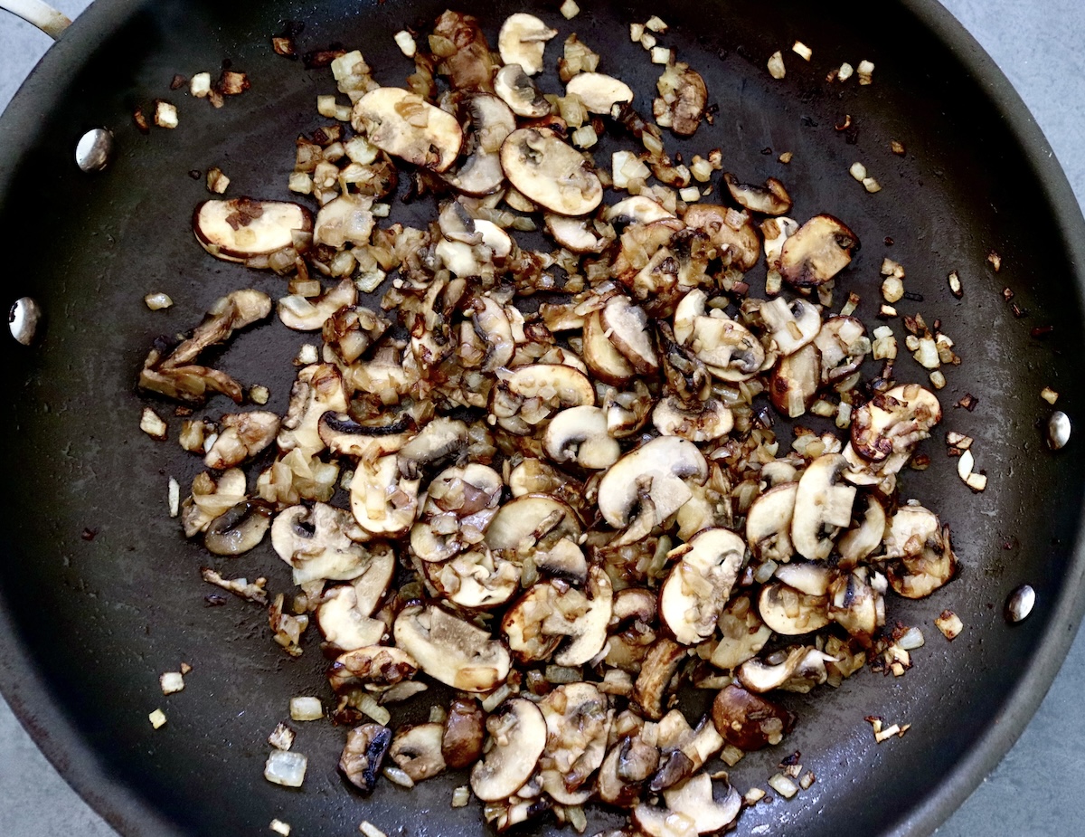 Skillet filled with chopped cooked mushrooms and chopped onions.