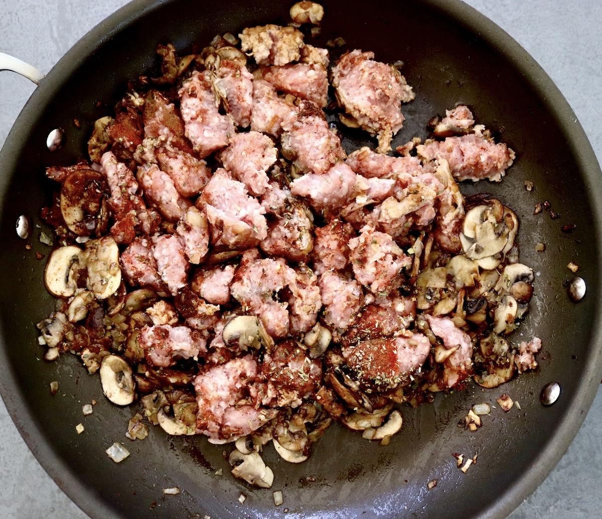 Raw pork, slices of cooked mushrooms and onions in a skillet.