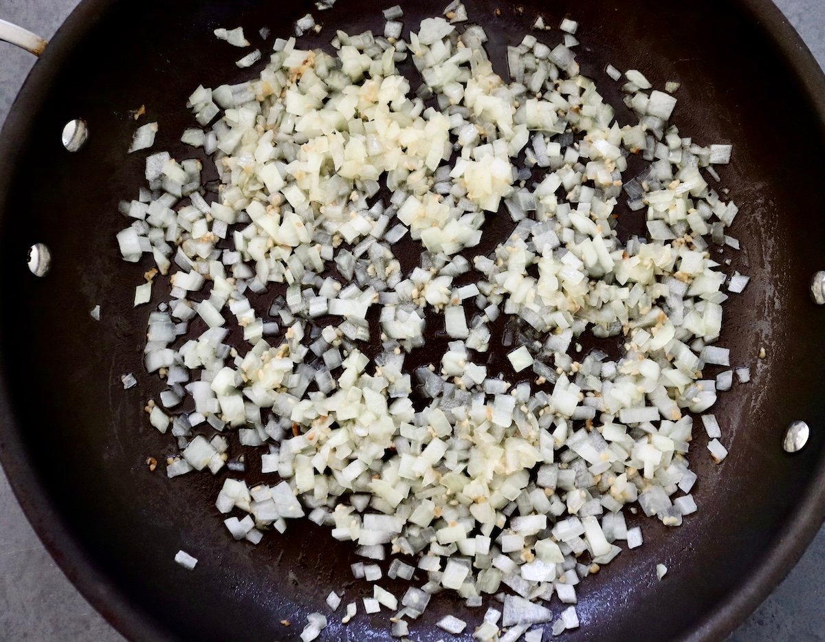 Dark skillet filled with sauteed diced onion and minced garlic.