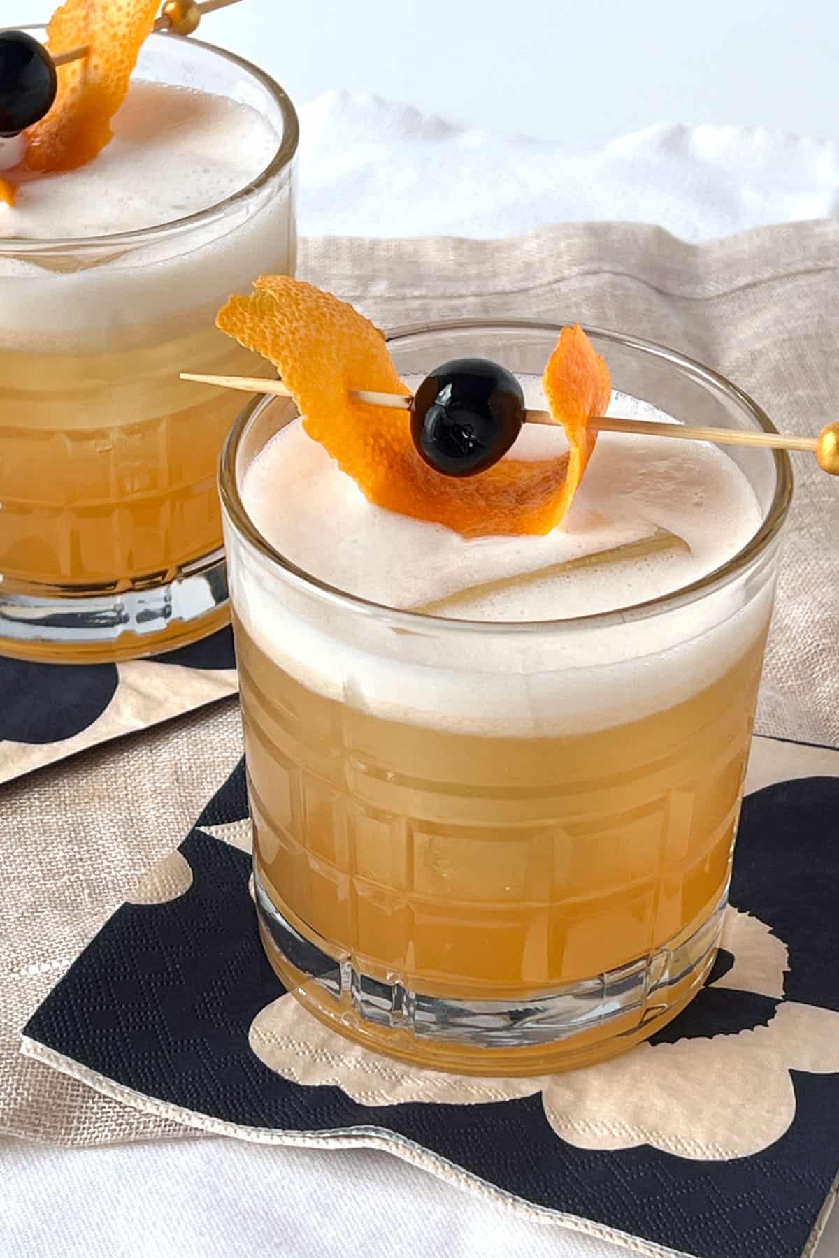 Whiskey bitters on the rocks in a tumbler with a cherry and orange peel garnish.