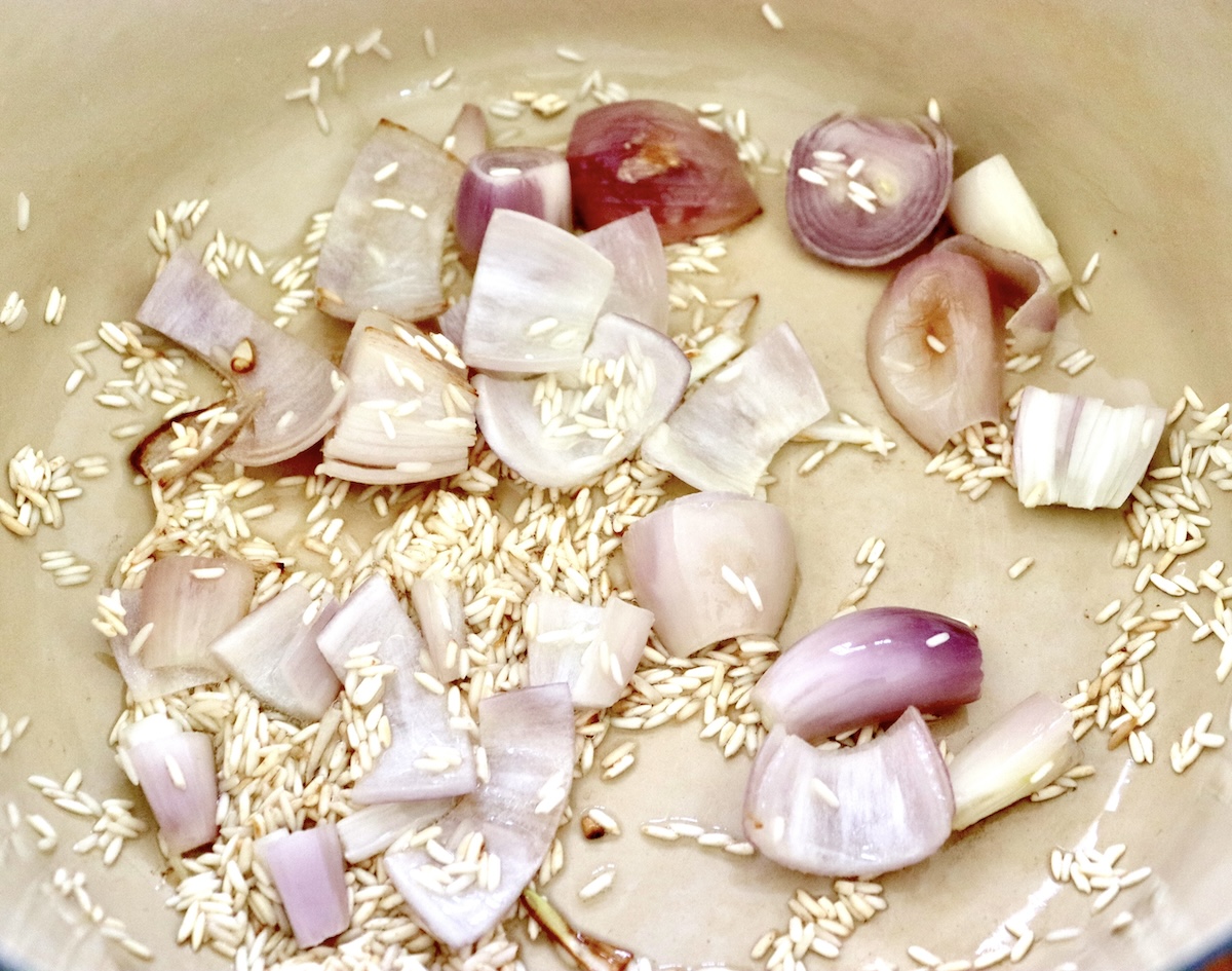 At the bottom of the dutch oven are half cooked shallots, sprinkled with golden rice and oil.
