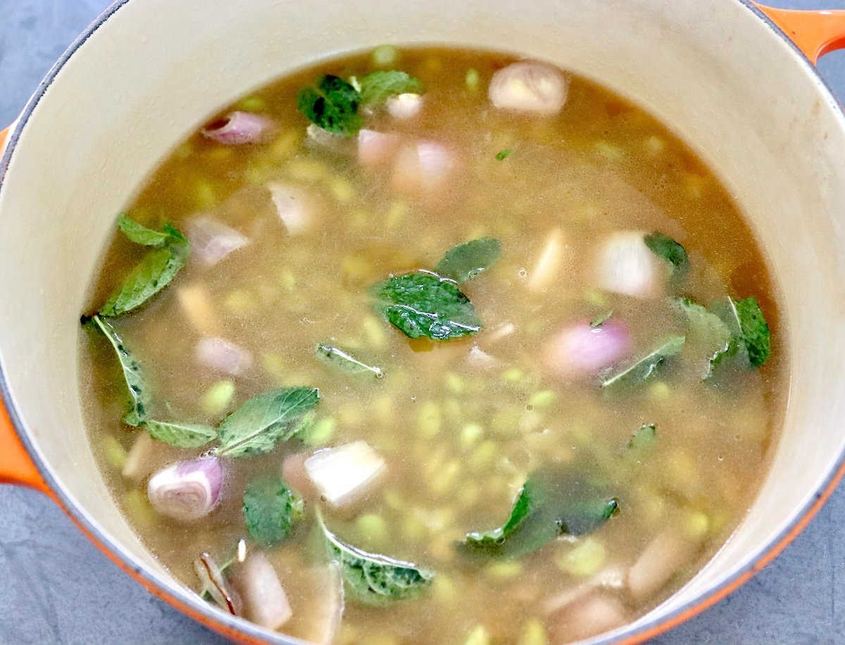 A Dutch oven filled with tomatoes, shallots, mint leaves and green vegetables.