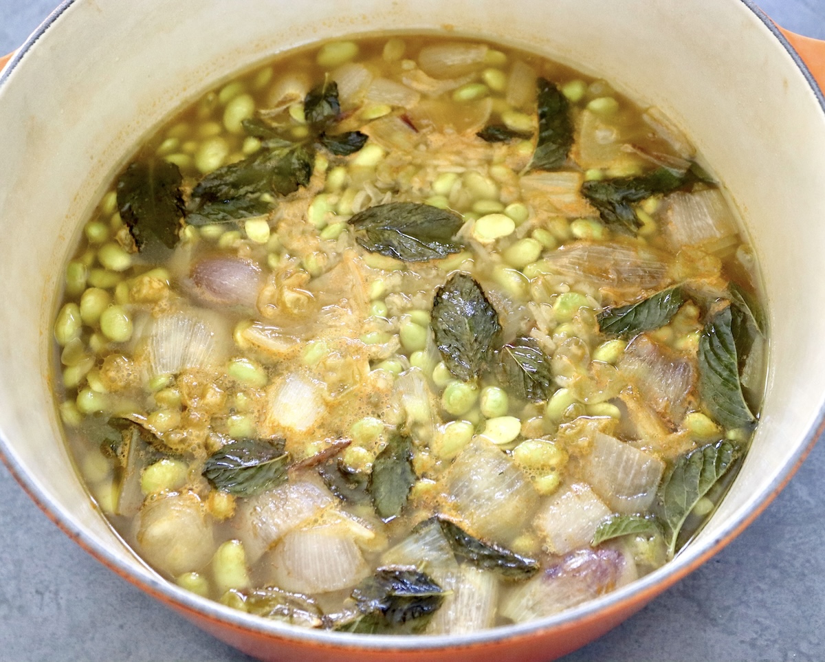 A dutch oven filled with steamed damame soup, with green mint leaves floating on top.