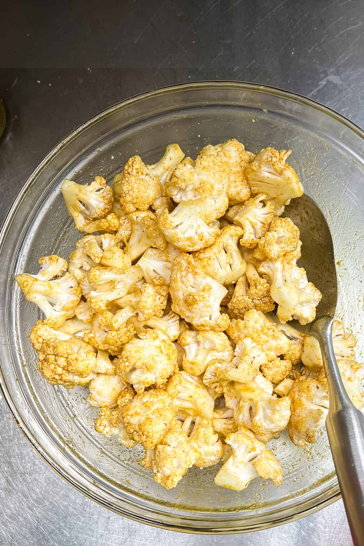 Cauliflower florets tossed with oil and curry powder, in a large mixing bowl.