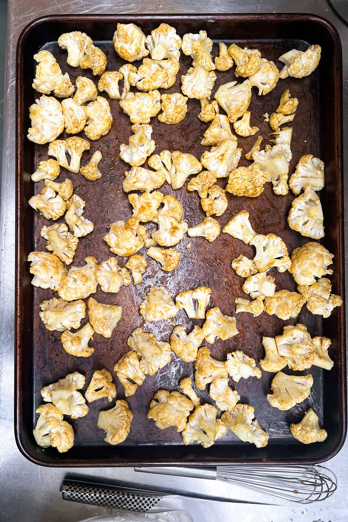 raw cauliflower florets coated with oil and curry powder, on a rimmed baking sheet.