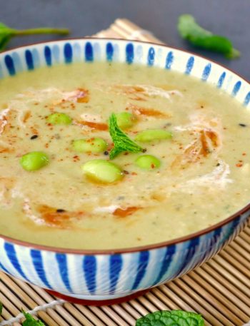 Blue and white striped, ceramic bowl with edamame soup with chili oil, mint leaf, and a bit of cream.