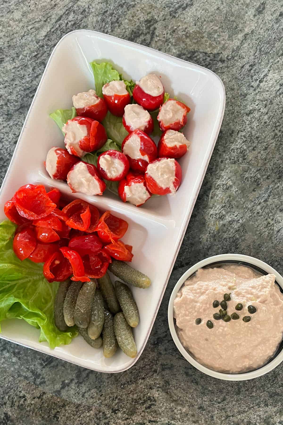 rectangular appetizer platter with a dozen or so peppadew peppers stuffed with tuna dip and a small bowl of tuna dip on the side, topped with capers.