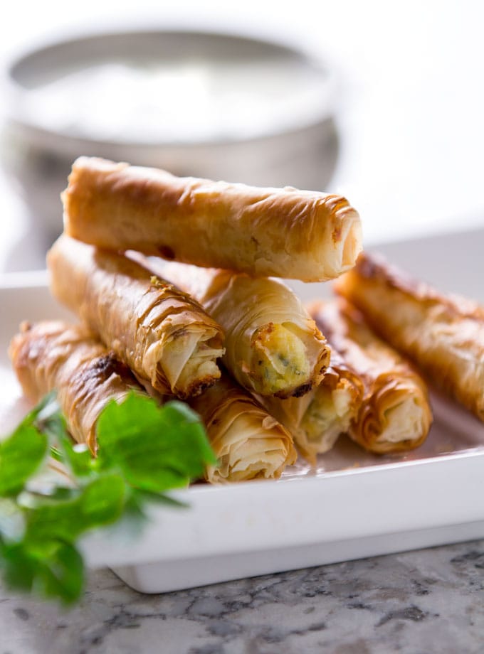Crisp, cheese-filled phyllo rolls stacked up on a small platter