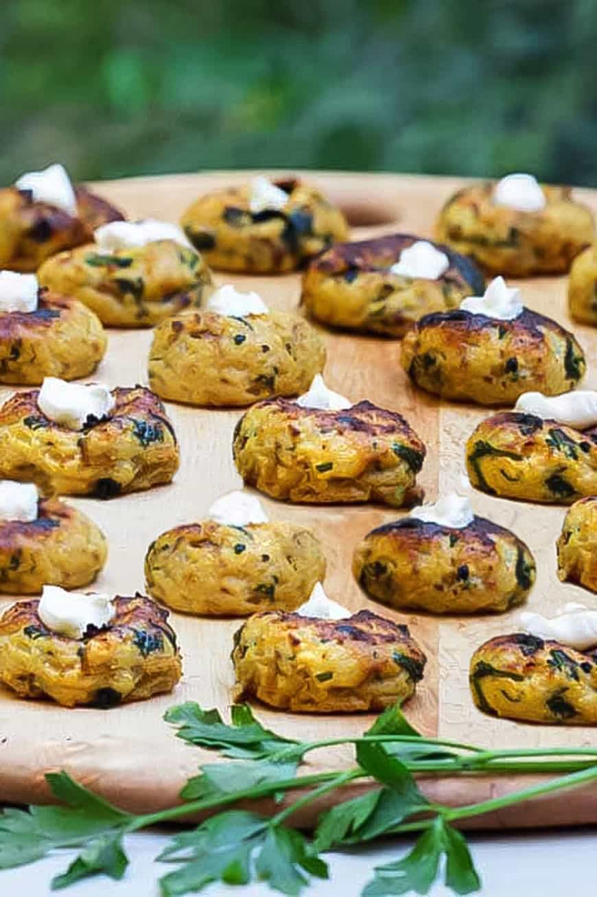 more than a dozen mini spinach and potato knishes with a dab of sour cream on each, sit on a wooden platter