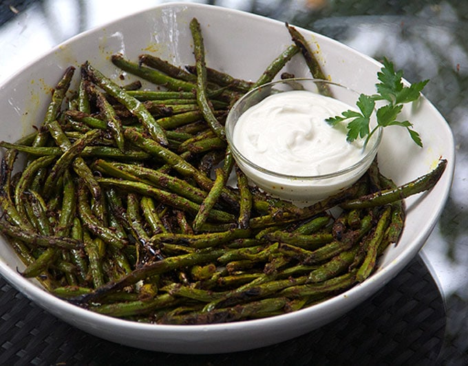 Serving bowl filled with blackened green beans surrounding a small bowl of yogurt dipping sauce.