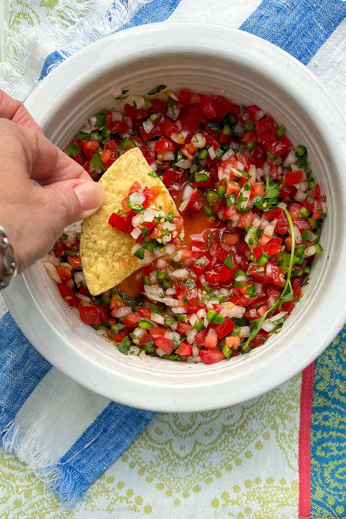 A corn tortilla chip being dipped into a bowl filled with finely chopped salsa fresca made from tomatoes, chilies, onion and cilantro.