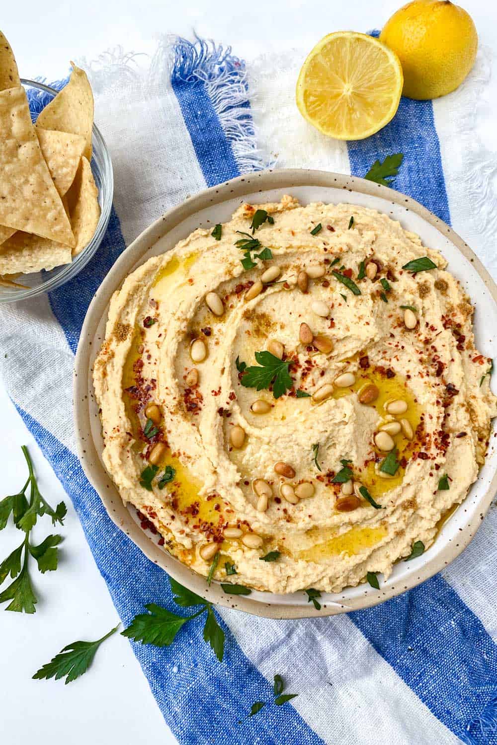 bowl of hummus toped with toasted pine nuts, olive oil drizzles and chopped parsley