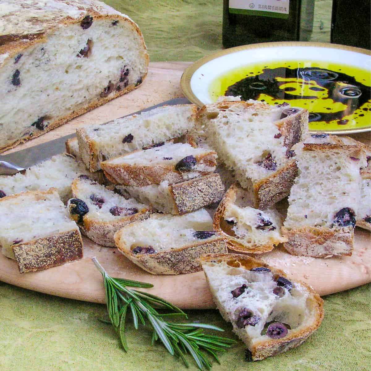Olive bread sliced and on a round wooden platter with olive oil and balsamic in a shallow bowl for dipping
