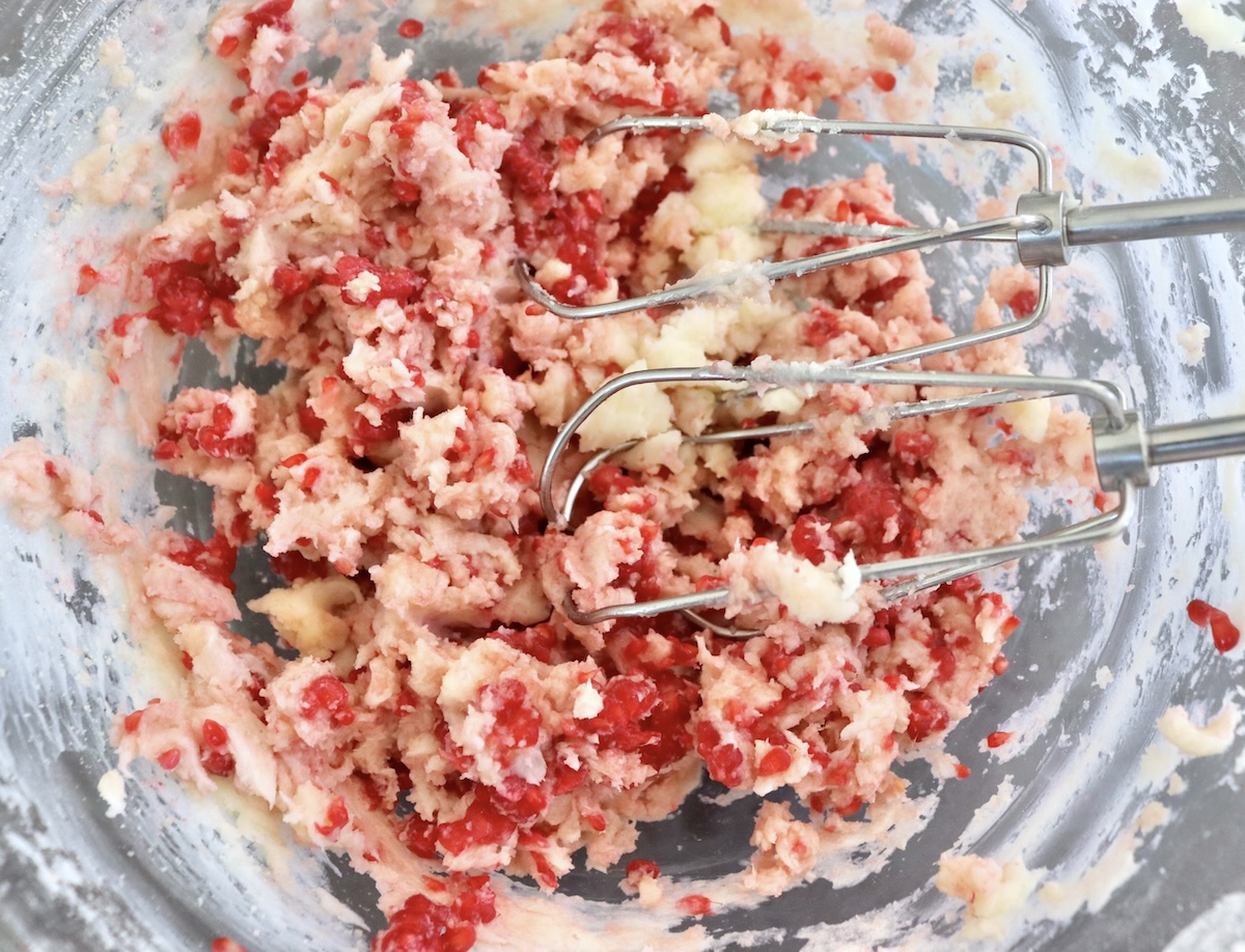 Raspberries are mixed in butter and sugar with an electric mixer in a glass bowl.
