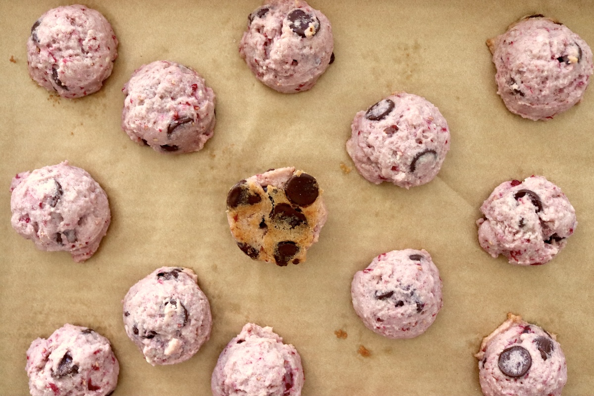 Several baked raspberry chocolate chip cookies on a parchment-lined baking sheet, one side down.