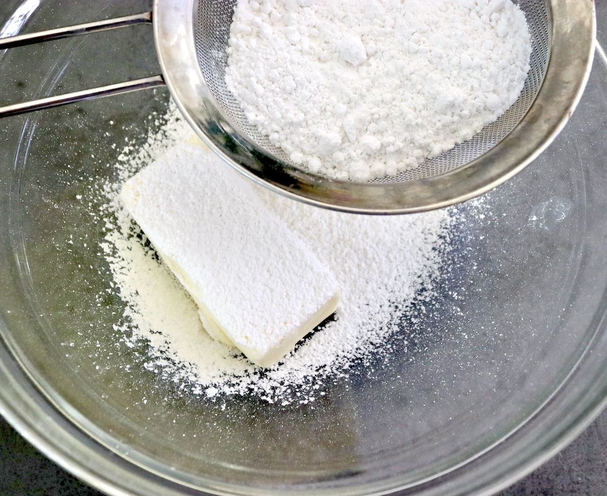 One stick of butter in a glass bowl with powdered sugar sifted over it.