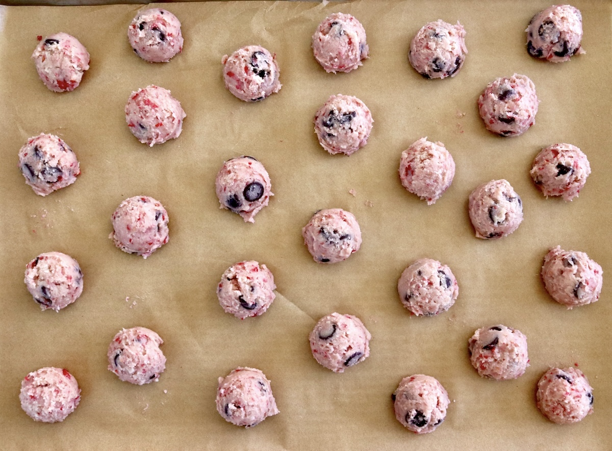 About a dozen balls of raspberry chocolate chip cookie dough on a parchment-lined sheet.