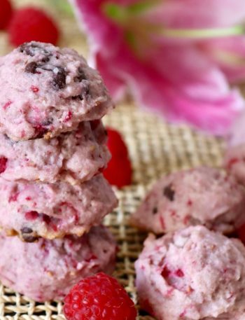 Stack of 4 raspberry chocolate chip cookies with a pink lily flower behind them, with a few fresh bright red raspberries around them.