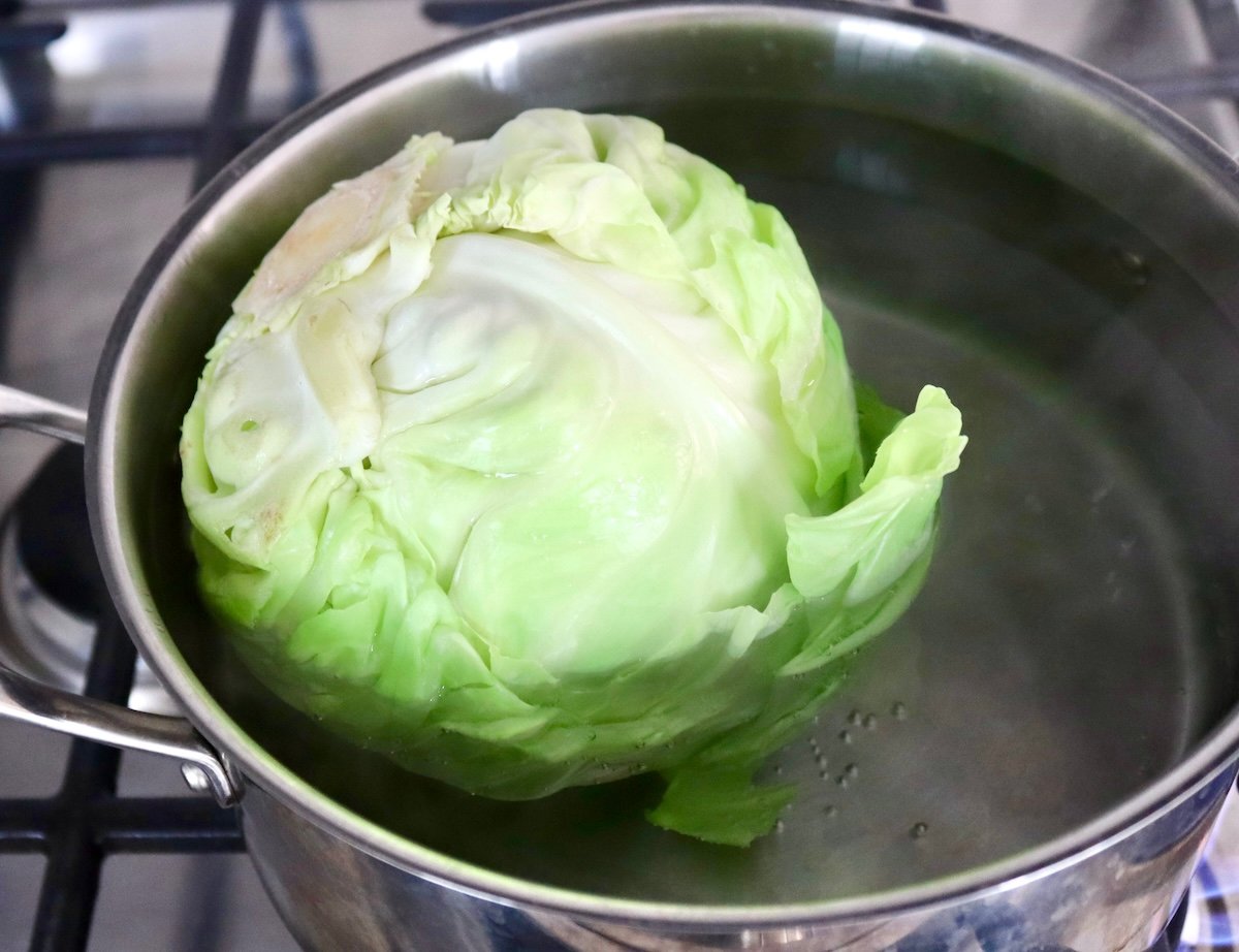 Large pot with water and whole head of green cabbage.
