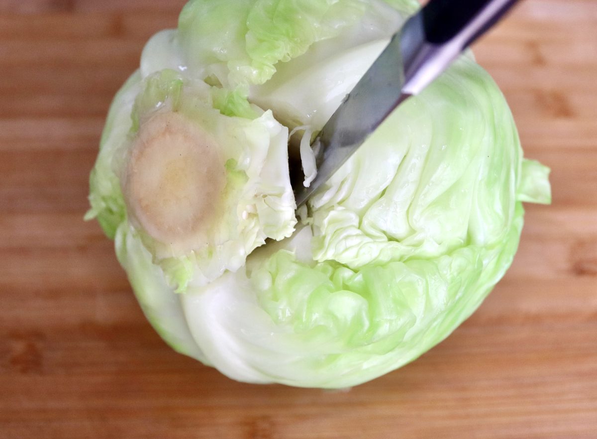 Whole green cabbage with paring knife sticking in it cutting out the root.