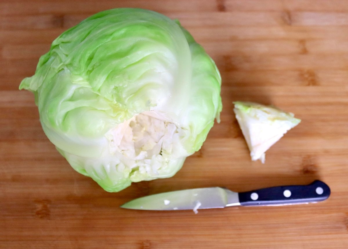 A whole head of green cabbage with the root cut out, and sitting next to it with a paring knife.