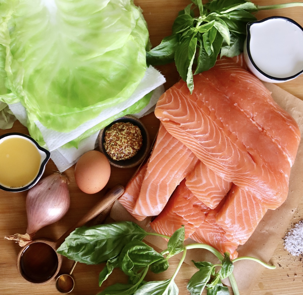 Ingredients for salmon and cabbage rolls including raw salmon fillets, blanched cabbage leaves, basil leaves, shallot, olive oil, honey, 1 egg, cream, mustard, and orange juice.