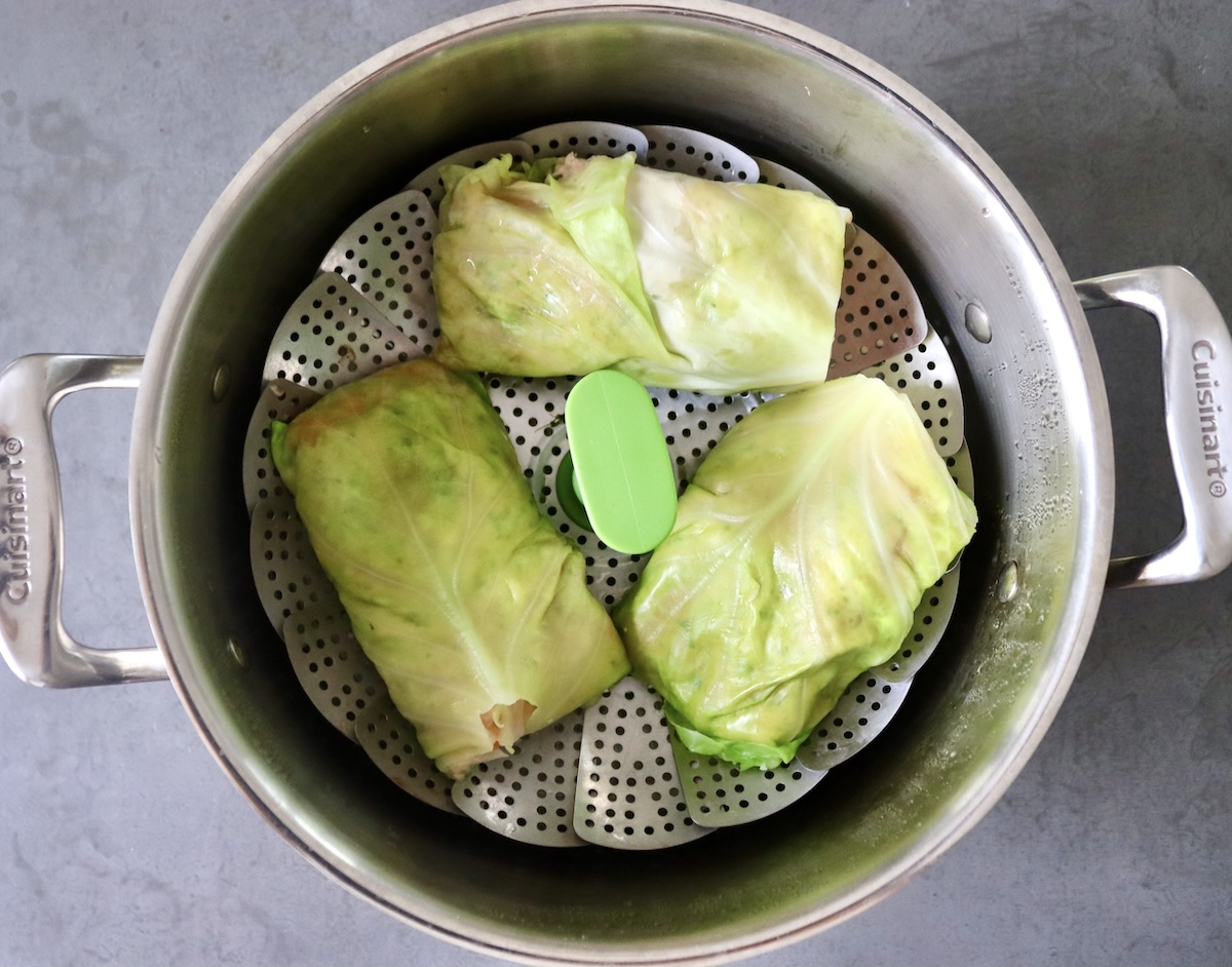 Three salmon-filled cabbage rolls in a steamer pot.