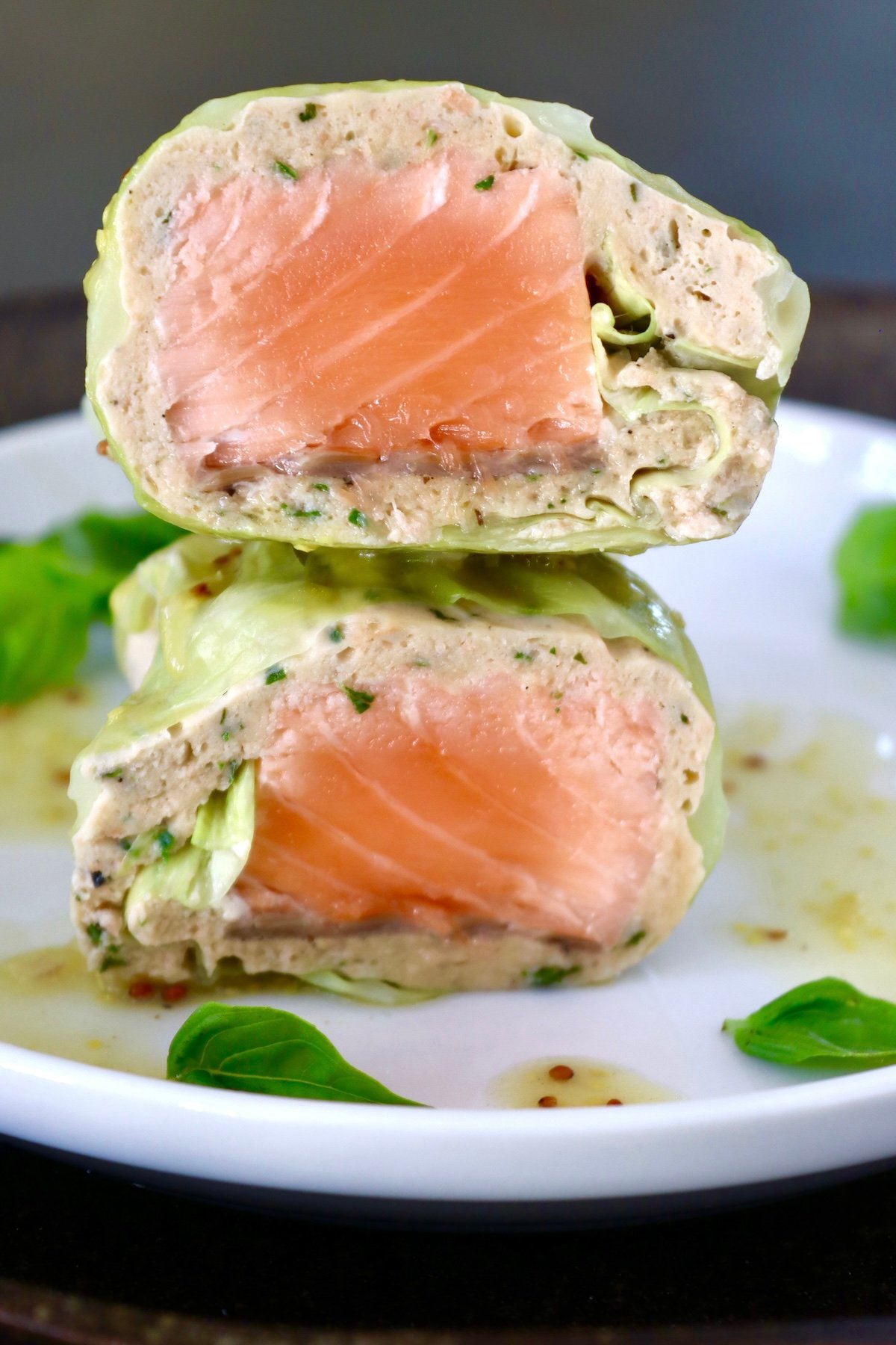 One salmon cabbage roll cut in half, with cross section shown on a white plate with basil leaves.