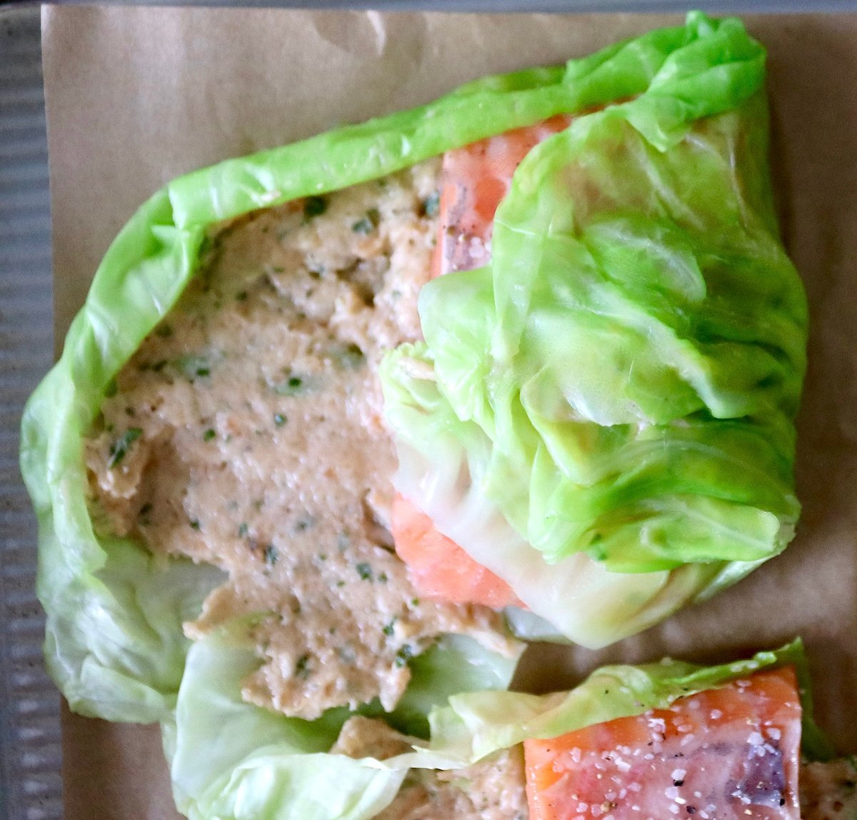 One cabbage leaf with salmon mousse being rolled over a fillet of salmon.