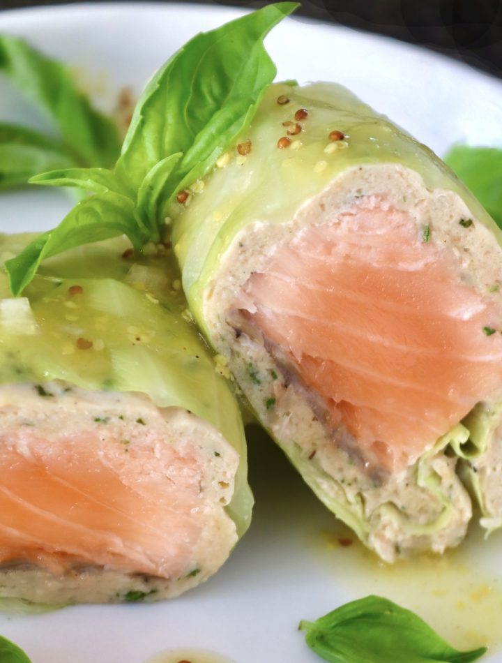 One Salmon Cabbage Roll sliced in half on a white plate with basil leaves and orange vinaigrette.
