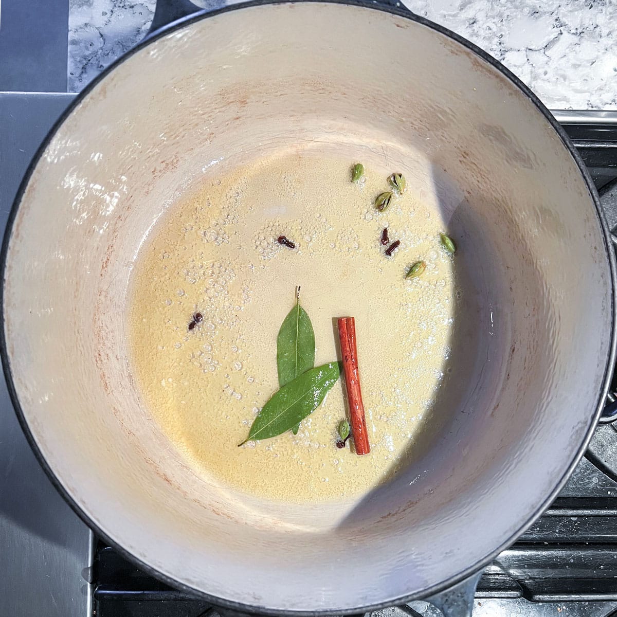 Dutch oven with whole spices simmering in olive oil.