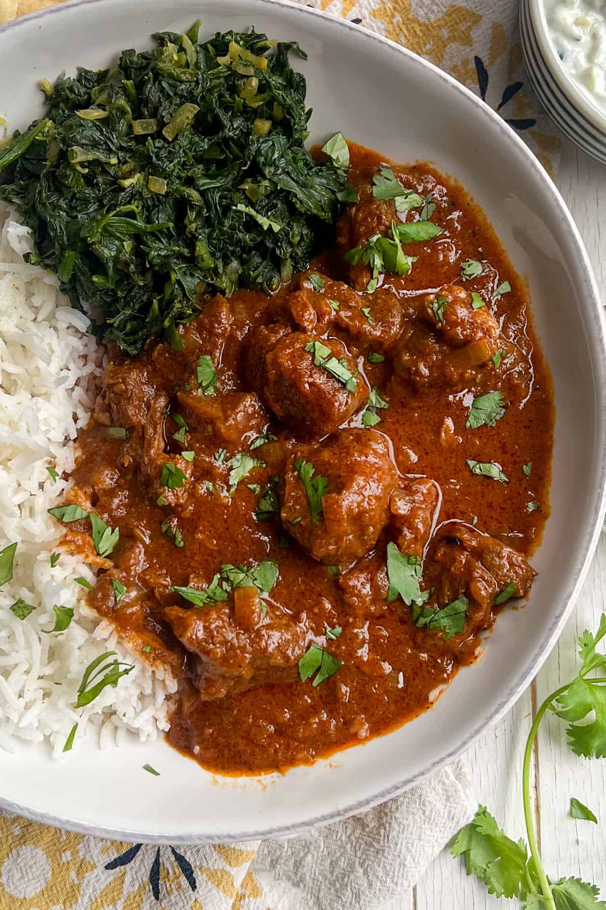 shallow bowl of lamb Rogan Josh with a side of spinach and rice.