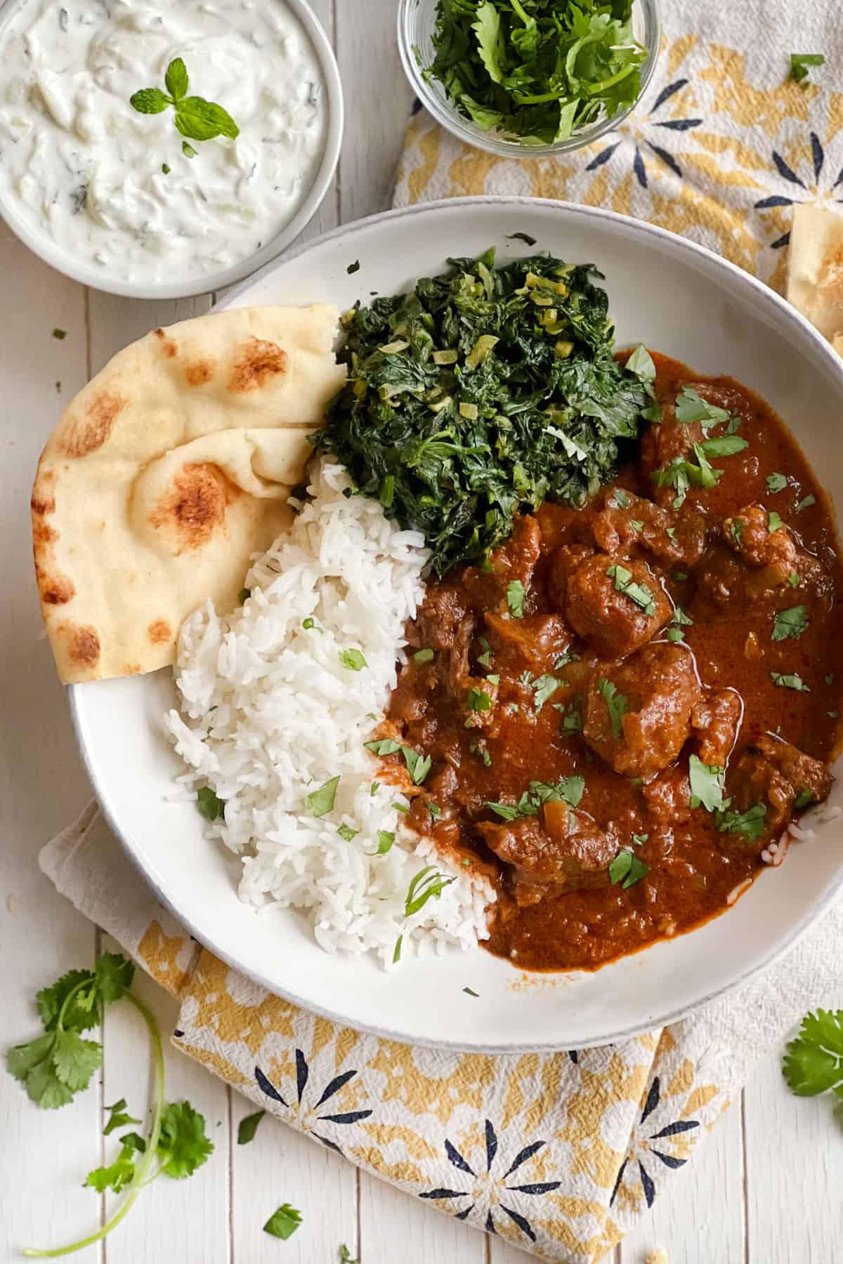 shallow bowl of lamb Rogan Josh with a side of spinach and rice.