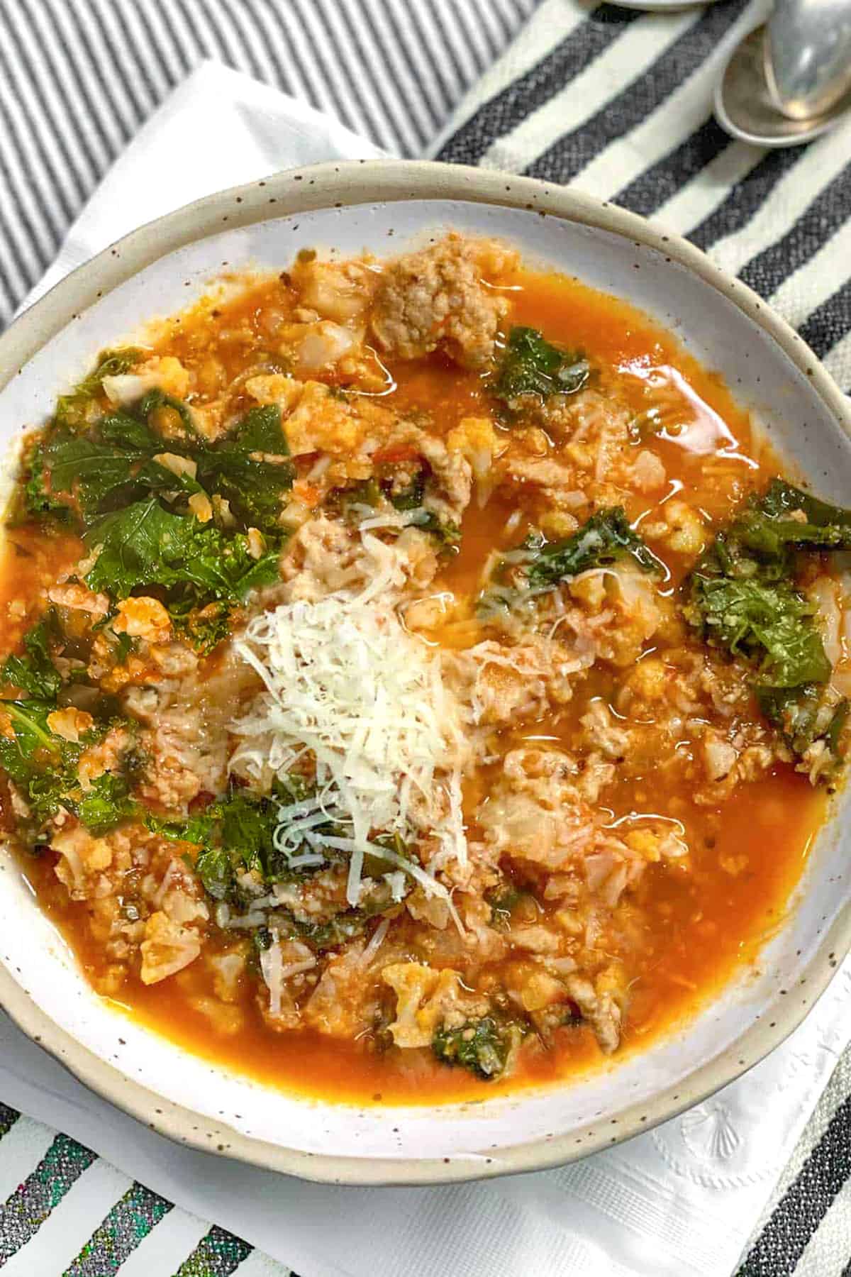 Ceramic bowl filled with tomato based soup with lots of ground turkey, chopped cauliflower and kale. Top with grated parmesan.