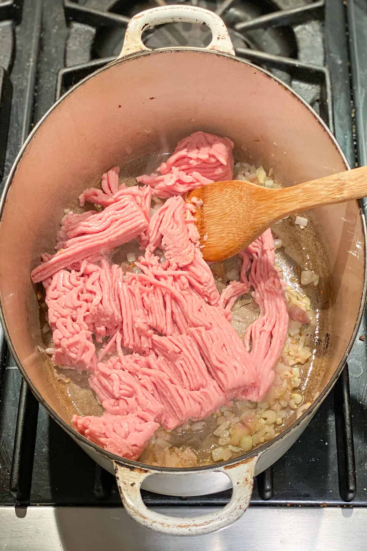 Raw ground turkey in a covered Dutch oven stirring with a wooden spoon.