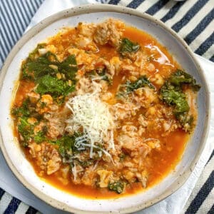 Ceramic bowl filled with ground turkey soup and kale, chopped cauliflower and tomato sauce. Top with grated parmesan.