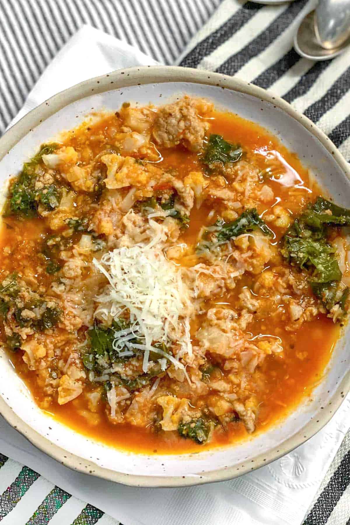 Ceramic bowl filled with tomato based soup with lots of ground turkey, chopped cauliflower and kale. Top with grated parmesan.