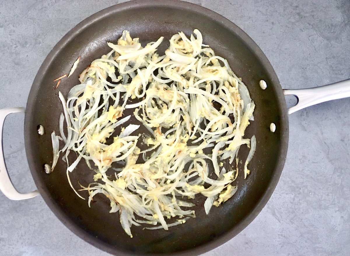 A large skillet with sauteed onion, ginger and garlic.