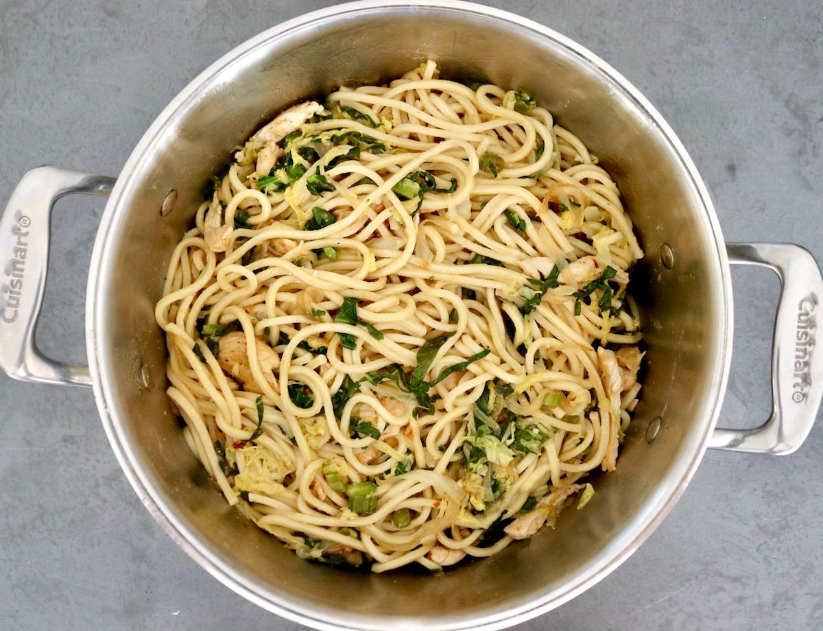 A large pot of steamed Chinese noodles mixed with fried cabbage, Gai Lan and spicy sauce.