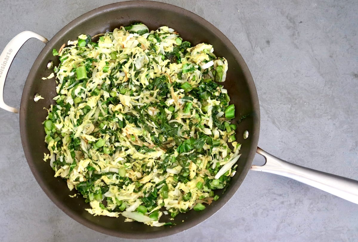 Cooked cabbage and Gai Lan, onion, garlic and ginger, in a large sauté pan.