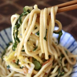 Serving Chinese Longevity Noodles with Gai Lan on a ceramic blue and white plate with a bite raised on chopsticks.