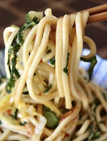 Serving of Chinese Longevity Noodles with Gai Lan on ceramic blue and white plate with a bite held up in chopsticks.