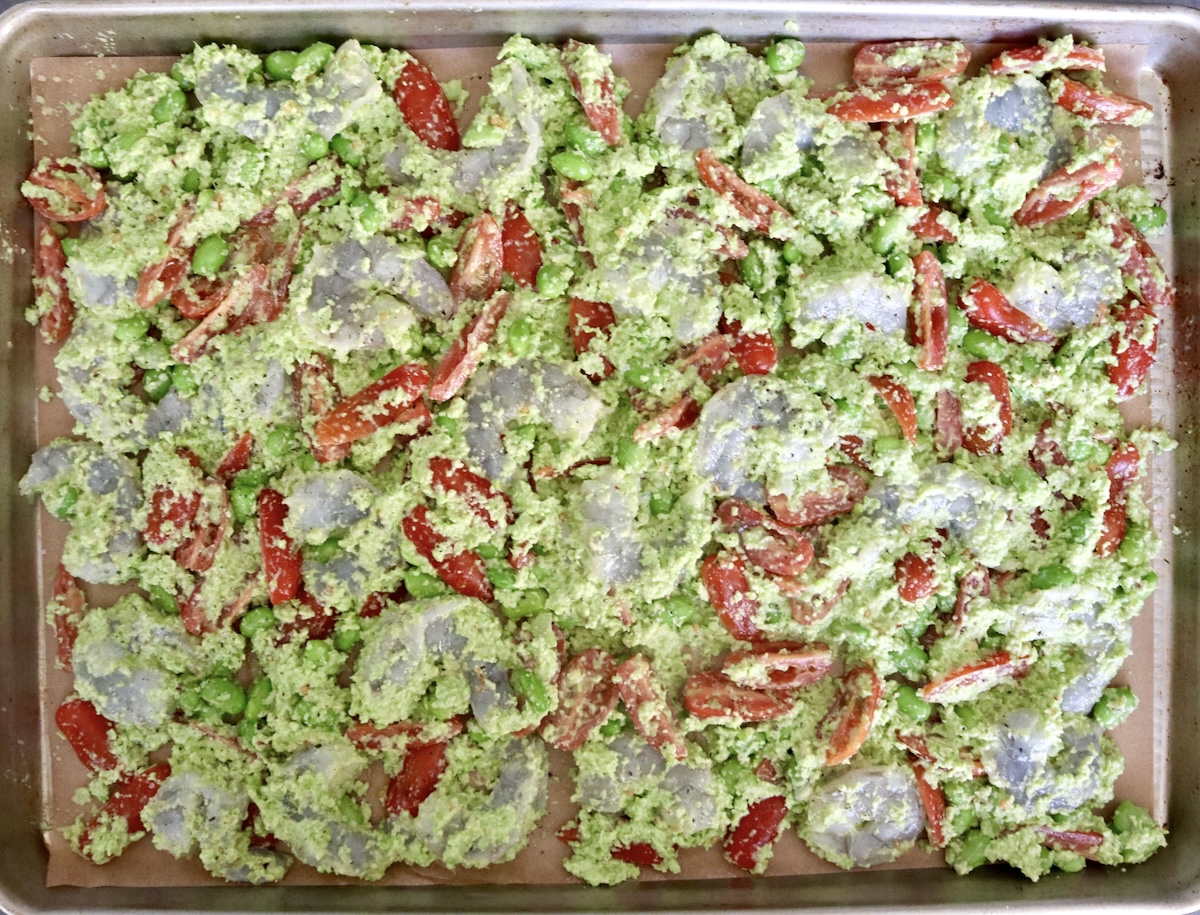 Sheet pan with an even layer of raw shrimp with edamame and chopped small tomatoes.