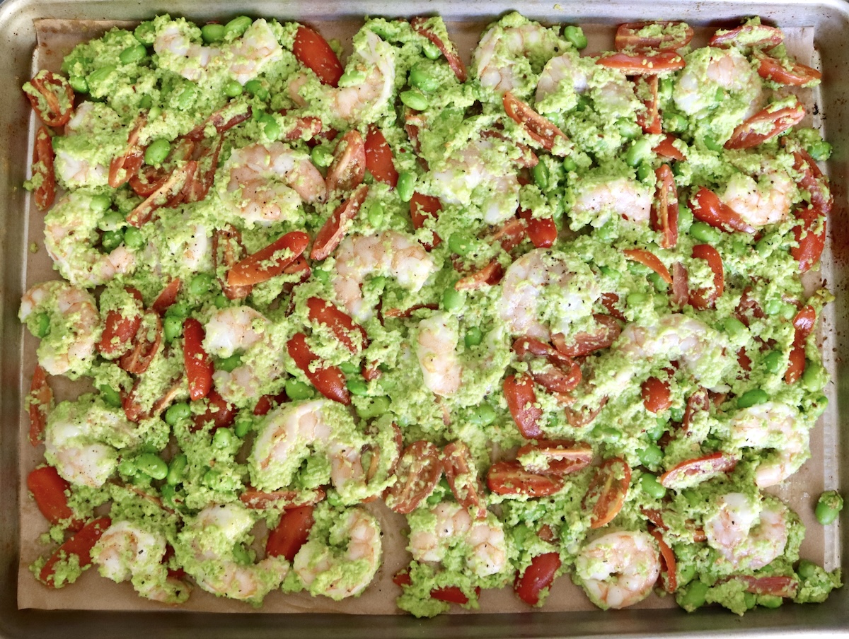 Sheet pan with an even layer of cooked shrimp with edamame and chopped small tomatoes.