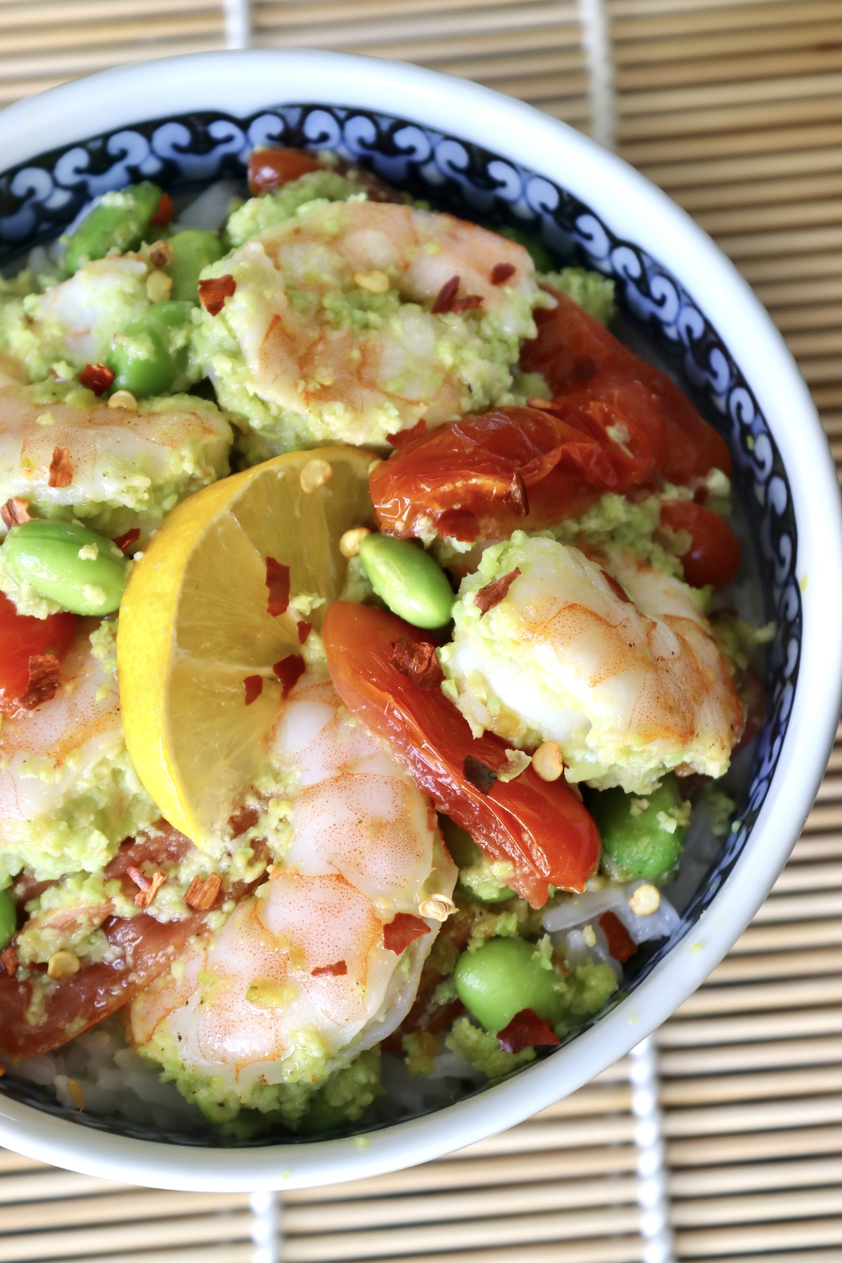 The top view is a ceramic bowl with colorful flowers, filled with shrimp, tomatoes and edamame over rice.