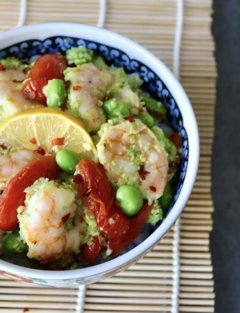 Ceramic bowl with colorful flowers on a sushi mat, filled with shrimp, tomatoes and edamame over rice.