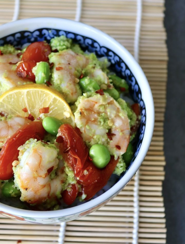Ceramic bowl with colorful flowers on a sushi mat, filled with shrimp, tomatoes and edamame over rice.