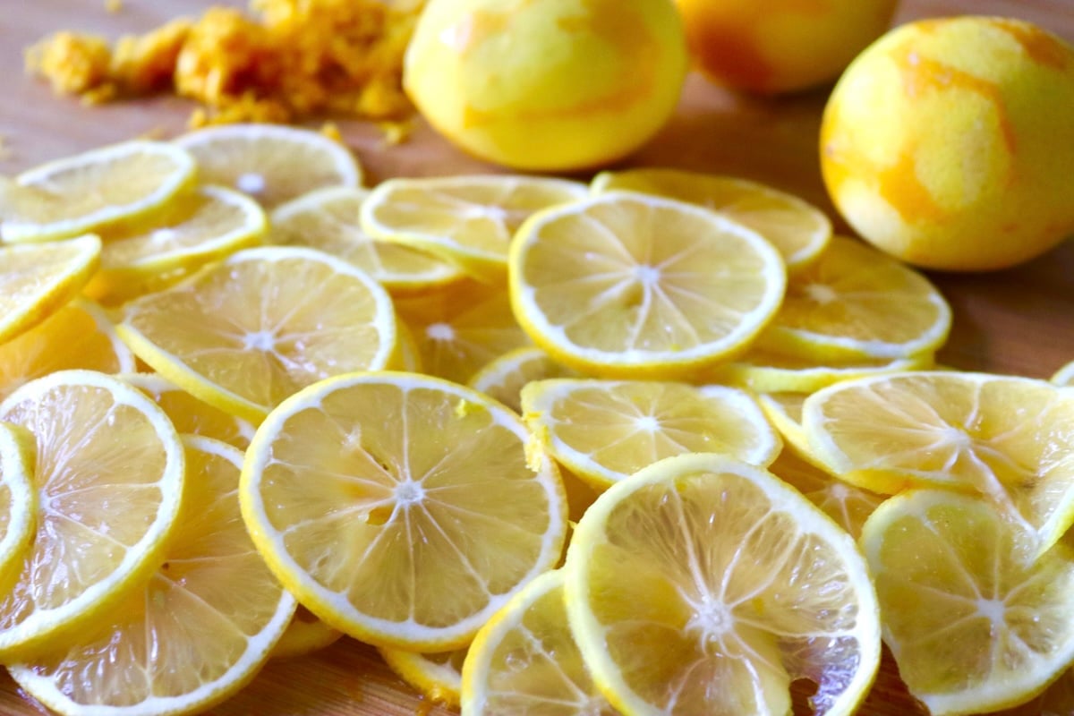 A cutting board full of very thinly sliced ​​lemons, several lemons and a pile of lemon zest.