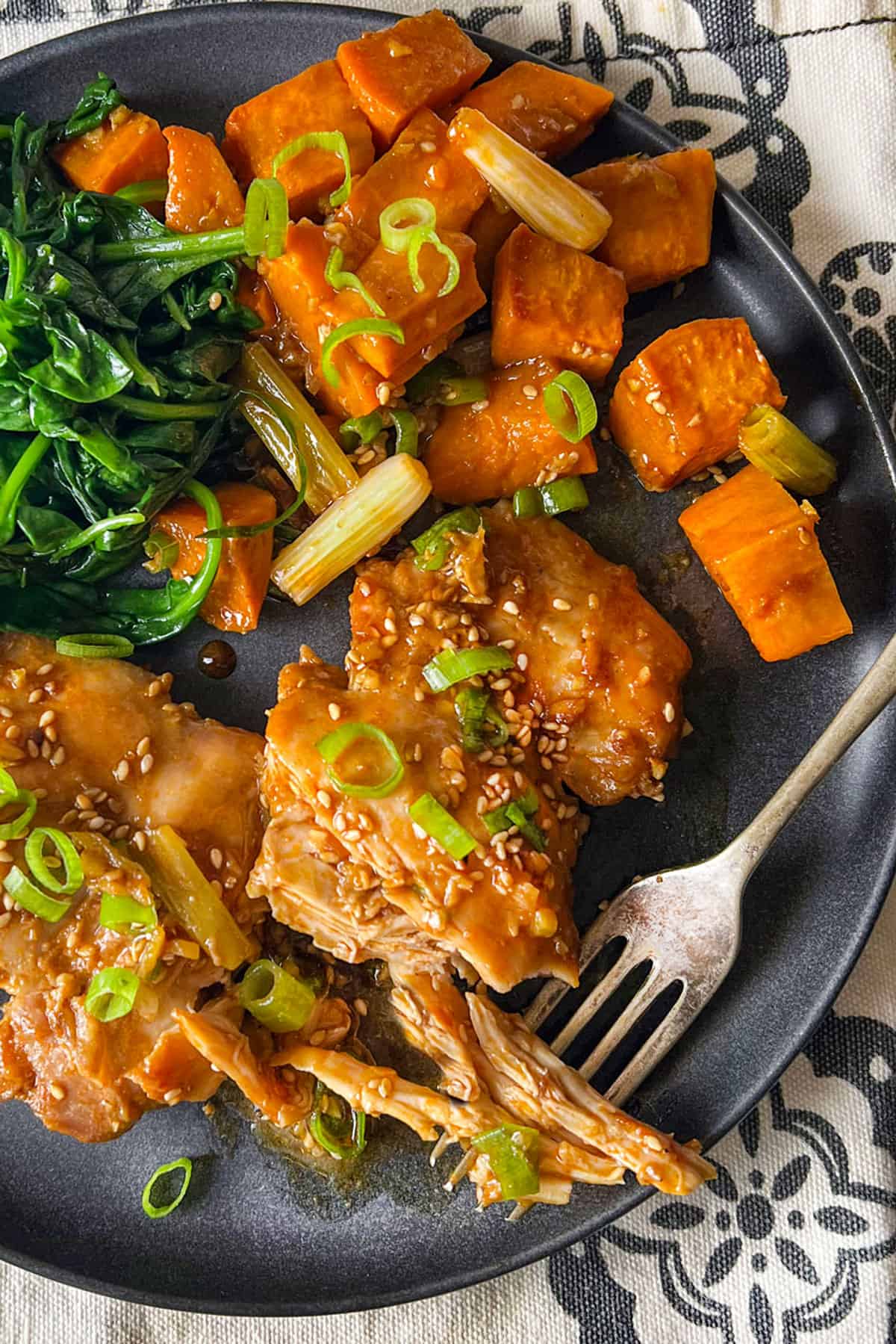 Two chicken thighs baked with roasted potato cubes and spinach cooked in a bowl.